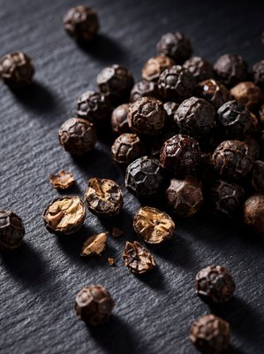[400×400px | 72dpi | JPG] Macro food photography: Malabar black peppercorns close-up, some whole showing wrinkled dark surface, some cracked open revealing lighter interior, arranged on dark slate, dramatic raking side light, ultra-sharp macro detail, editorial style, no text
